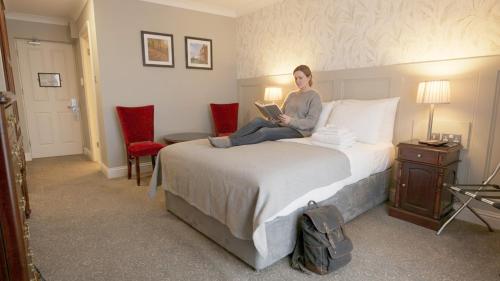 a woman sitting on a bed reading a book at Killarney Riverside Hotel in Killarney