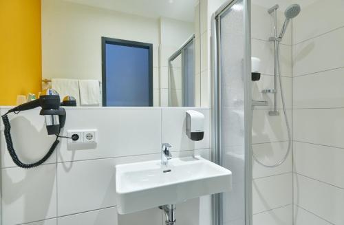 a white bathroom with a sink and a shower at McDreams Hotel Wuppertal City in Wuppertal