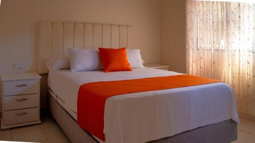 a bedroom with a large bed with an orange pillow at Hotel ALCALA in Mingueo