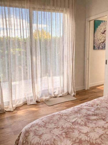 ein Schlafzimmer mit einem großen Fenster mit weißen Vorhängen in der Unterkunft The Tiny Abode in Snells Beach