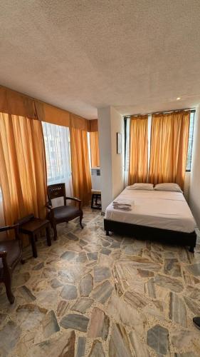 a bedroom with a bed and a chair and windows at Hotel Montecarlo in Cali
