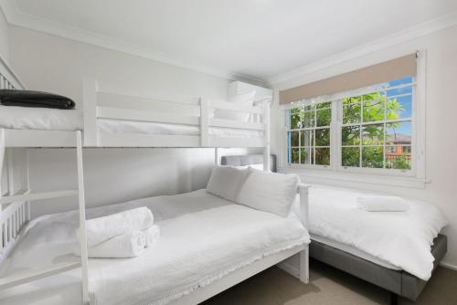 a white bedroom with two bunk beds and a window at Coastal Blue in Windang