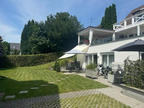 a white house with an umbrella and a yard at Bodenseeapartments Kunst & Design in Immenstaad am Bodensee