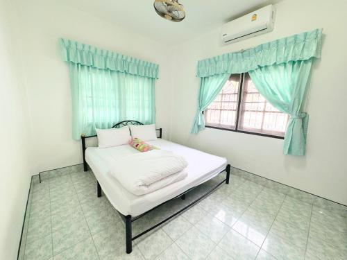 a bedroom with a white bed with blue curtains and a window at Vacation Home Tambon Karon in Karon Beach