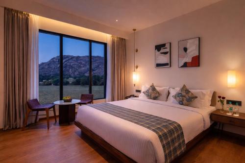 a hotel room with a bed and a large window at Avisa Hotel & Resort Abu Road - Luxury Pool & Mountain View in Ābu Road