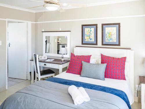 a bedroom with a bed with red pillows and a desk at Mount Currie Inn in Kokstad