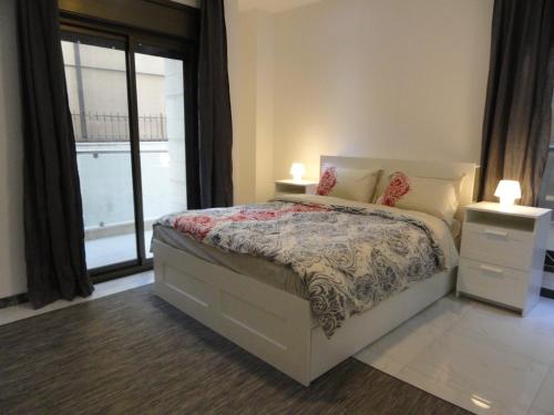 a bedroom with a bed with two night stands and a window at Diyarkom Apartment in Amman