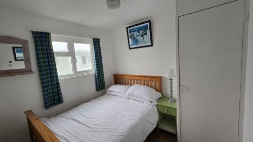 a small bedroom with a bed and a window at Chalet 151, Perran Sands in Perranporth