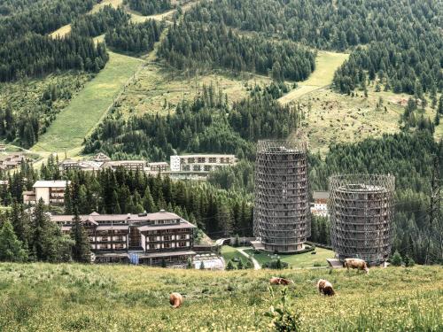two tall buildings on a hill with cows in a field at Falkensteiner Residences edelweiss in Katschberghöhe