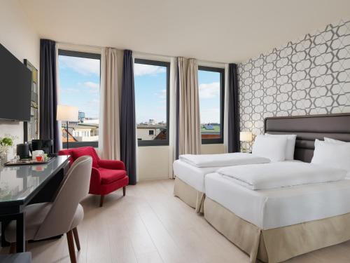 a hotel room with two beds and a red chair at H10 Berlin Ku'Damm in Berlin