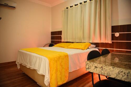 a bedroom with a bed with yellow sheets and a table at Hotel Volp Patos in Patos de Minas