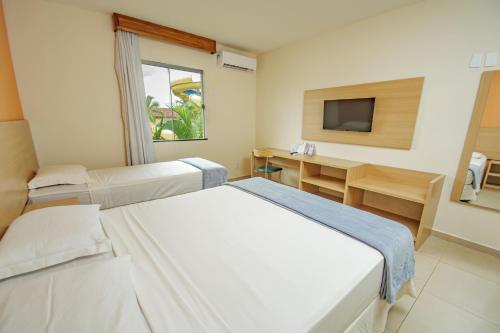 a room with two beds and a desk and a television at Portobello Park Hotel in Porto Seguro
