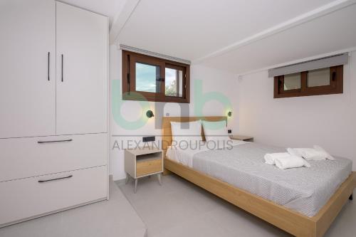 a white bedroom with a bed and a window at Elaion House in Agia Paraskevi