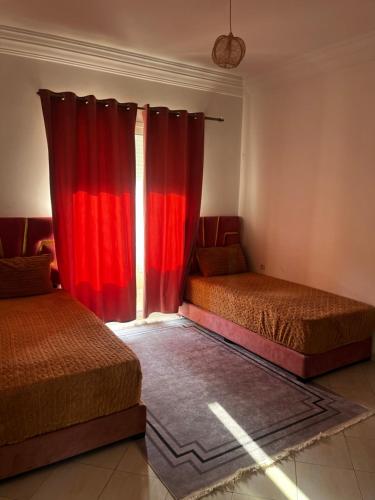 two beds in a room with red curtains at Appartement Moderne à coté de la plage - Essaouira in Essaouira