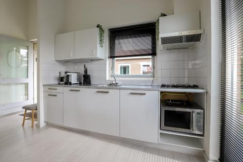 a white kitchen with white cabinets and a microwave at Rekerlanden 275 in Warmenhuizen