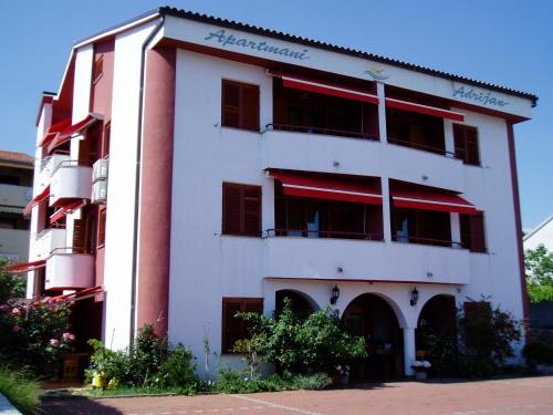 a white building with red shuttered windows at Apartmani Adrijan Krk in Krk