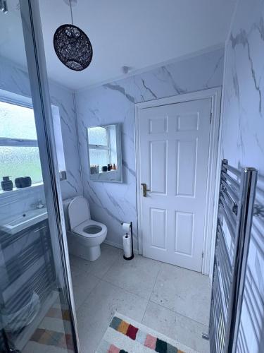a white bathroom with a toilet and a door at Bide A While at the Port in Portrush