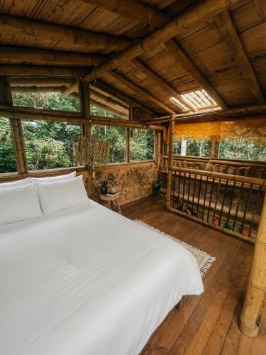 a bedroom with a white bed in a room with windows at Bosque Hondo Ecoliving in Medellín