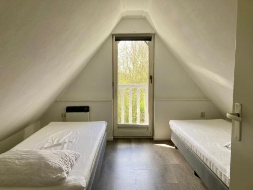 a attic bedroom with two beds and a window at Olivia 6pers House with a private garden close to the National Park Lauwersmeer in Anjum