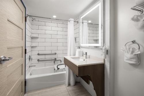 a white bathroom with a sink and a tub and a mirror at Spark by Hilton Virginia Beach Oceanfront in Virginia Beach