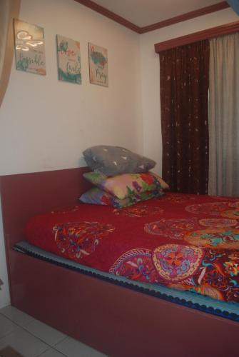 a bed with a red blanket and pillows on it at Charm Condo Just Steps from Enchanted Kingdom Sargas in Santa Rosa