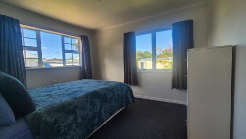 a bedroom with a bed and two windows at Bach 30 at Waimārama Beach in Waimarama