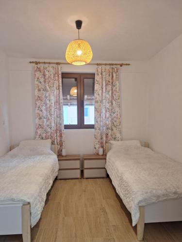 two beds in a bedroom with a window and a chandelier at Vila Dragica in Bogutovac