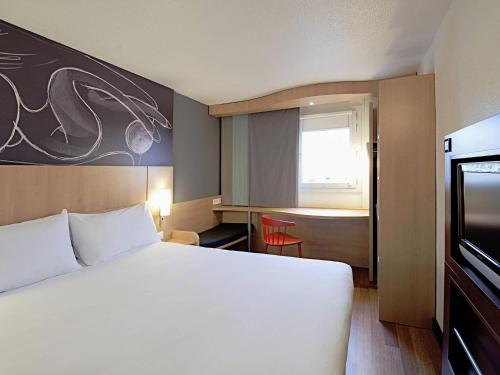 a hotel room with a large white bed and a window at ibis Soissons in Soissons