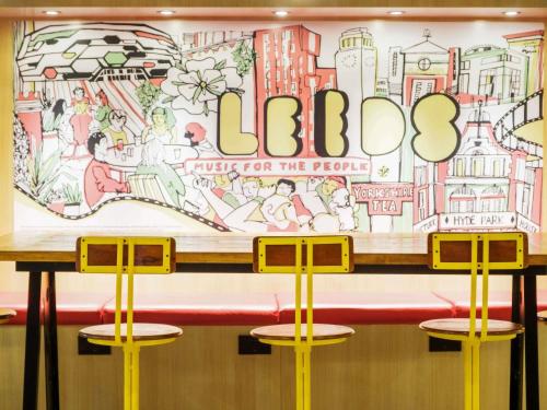 a table with three stools in front of a mural at ibis Styles Leeds City Centre Arena in Leeds