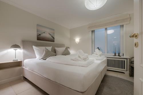 a white bedroom with a large white bed and a window at Appartement Lycka in Keitum