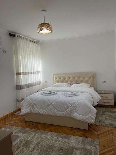 a white bedroom with a large bed and a chandelier at Apartament Qetesia in Çorovodë