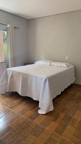 a white bed in a bedroom with a wooden floor at Chalés ninhos do cerrado in Cavalcante