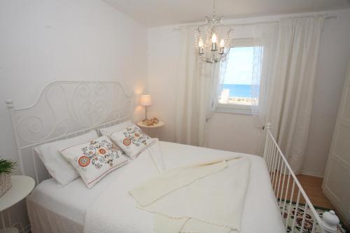 een witte slaapkamer met een bed met een kroonluchter en een raam bij Apartments Abbazia in Bibinje