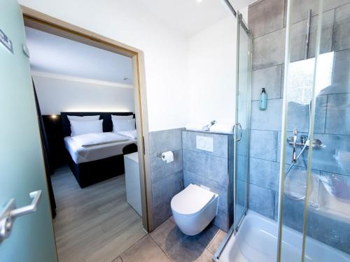 a bathroom with a toilet and a shower and a bed at DORMERO Hotel Aalen in Aalen