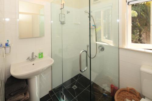 a bathroom with a sink and a glass shower at Little Palm Beach Hideaway in Waiheke Island
