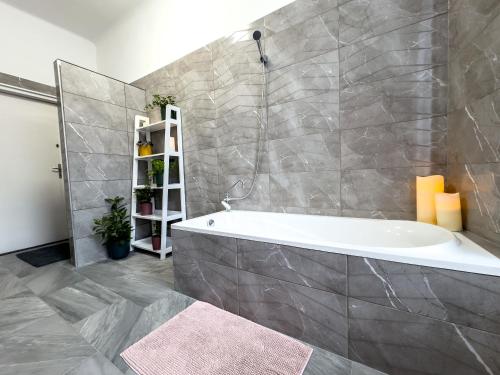 a bathroom with a bath tub and a tile wall at Flamingo Rezidencia Apartman in Eger