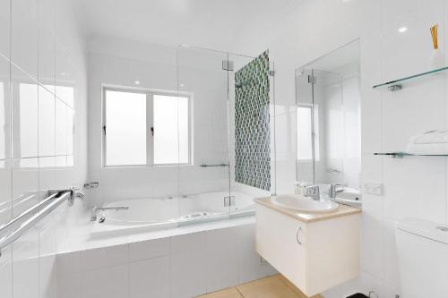 a white bathroom with a tub and a sink and a bath tubermott at 19 Colonial in Noosaville