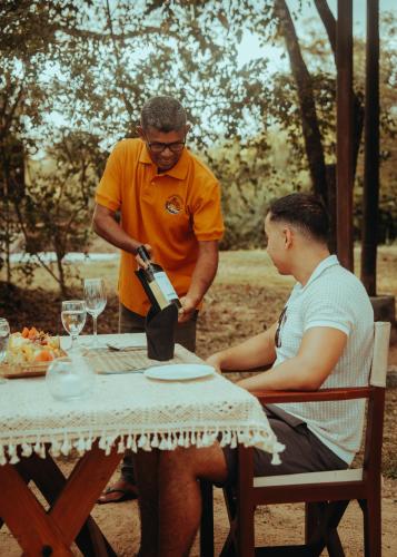 a man pouring a man a bottle of wine at a table at Chena Wilds Wilpattu in Horuwila