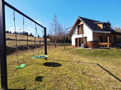 a playground with swings in front of a house at Leśna Chata domek z balią in Sękowa