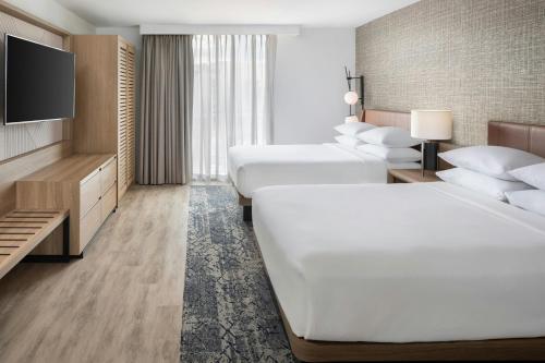 a hotel room with two beds and a flat screen tv at Sheraton Suites Fort Lauderdale at Cypress Creek in Fort Lauderdale