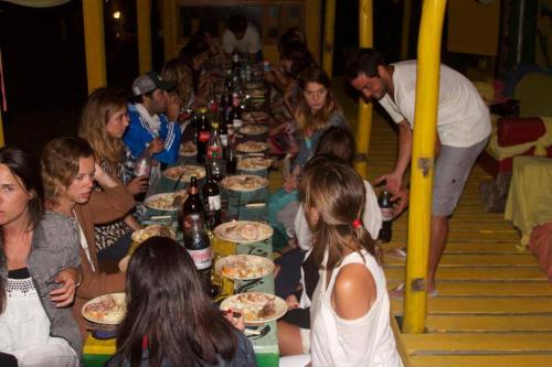 un grupo de personas sentadas alrededor de una larga mesa con pizza en Hostel Francisca, en La Pedrera