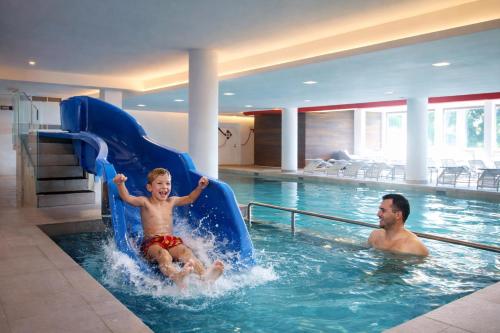 a man and a child on a slide in a swimming pool at CASA IBEX - Residence Veronza con piscina, Dolomiti Affitti in Cavalese