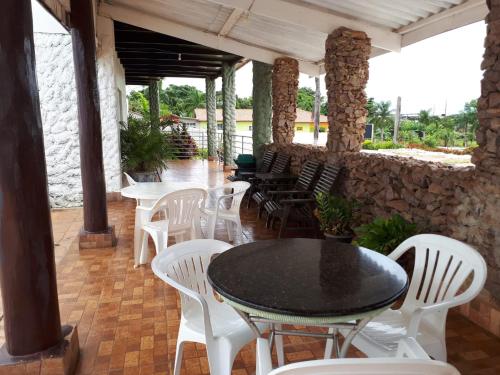 a patio with white chairs and tables and a stone wall at Hotel Pousada das Palmeiras in Colíder