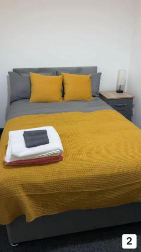 a bed with a yellow blanket and a book on it at PLUS Properties Eastwood 1 in Stoke on Trent