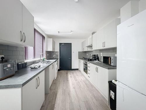 a kitchen with white cabinets and a wooden floor at PLUS Properties Eastwood 1 in Stoke on Trent