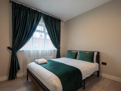 a bedroom with a bed with green curtains and a window at Spacious 2-Bedroom Flat in Worcester Park