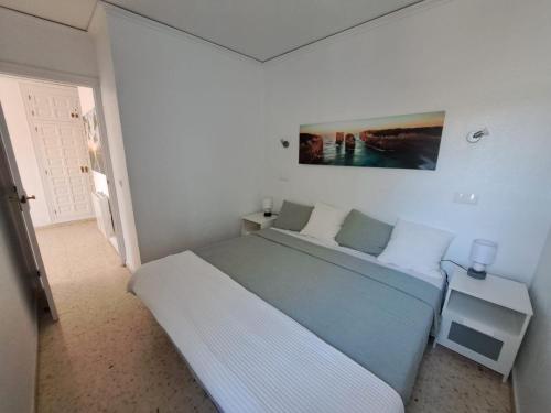 a white bedroom with a bed and a painting on the wall at Appartement El Palmar Denia in Denia