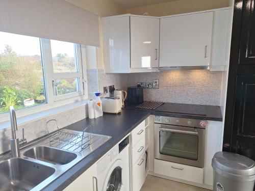 a kitchen with white cabinets and a sink and a dishwasher at Gweedore Seaview Cottage in Bun na Leaca