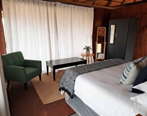 a bedroom with a bed and a chair and a table at Chobe Lesoma Chalets Hotel in Lesoma