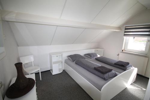 a white bedroom with a bed and a chair at Geuldal Guest Apartments in Valkenburg